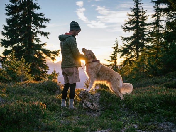 A hiker pets his dog at sunset in the mountains.