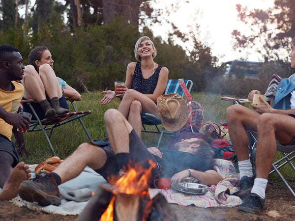 Group of friends on camping trip, by the lake with tent and making bonfire