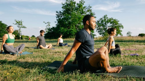 A group of people practicing yoga in a park on a sunny summer evening