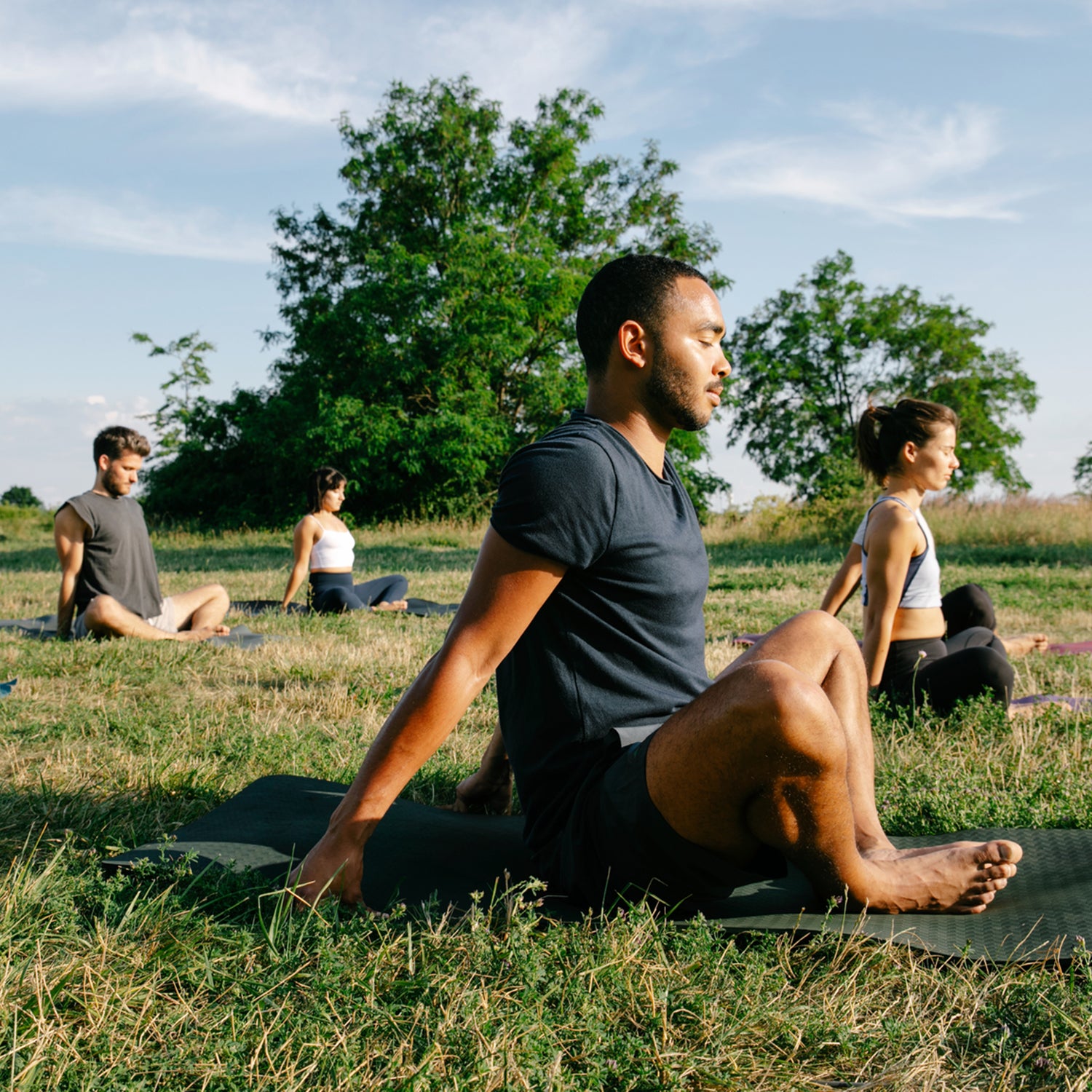 A group of people practicing yoga in a park on a sunny summer evening