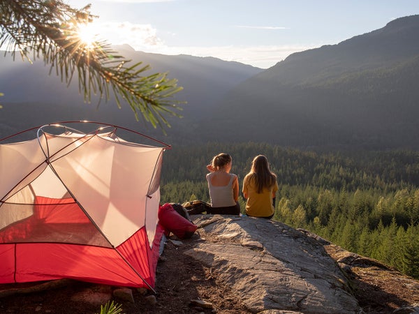 Young women watch the sunset on a mountain ledge campsite