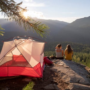 Young women watch the sunset on a mountain ledge campsite
