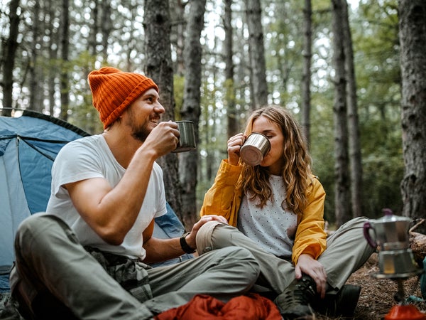Low angle view of young male and female friends sitting on blanket on ground outside tent during hiking and drinking coffee