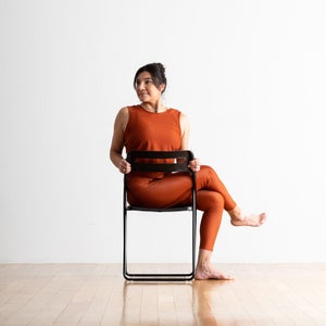 Dark haired woman practices Half Lord of the Fishes in a black chair.