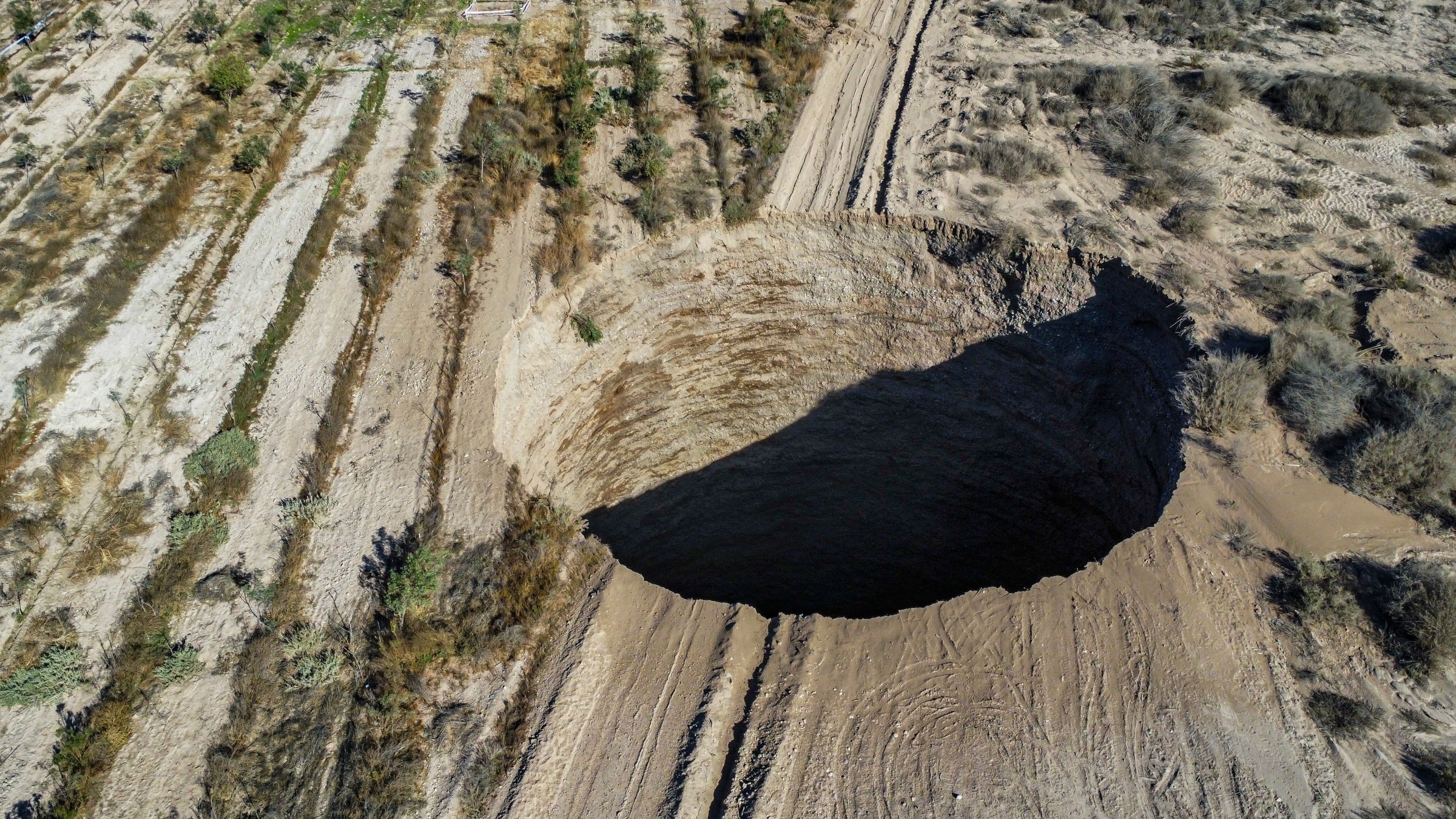 An overhead view of the Chilean sinkhole. It is a large, seemingly endless hole in the middle of a road in a desert landscape.