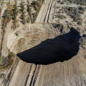 An overhead view of the Chilean sinkhole. It is a large, seemingly endless hole in the middle of a road in a desert landscape.