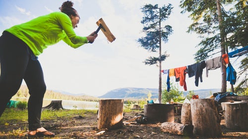 A young woman uses a hatchet to chop wood