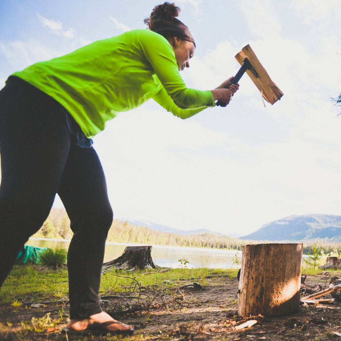 A young woman uses a hatchet to chop wood