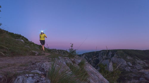 A solo trail runner at dusk with a headlamp