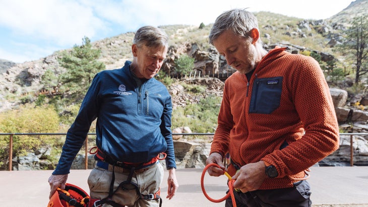 Two men harnessing up to rock climb outdoors