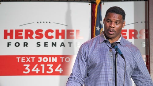 Herschel Walker speaks in front of a red, white, and black campaign sign that says, 