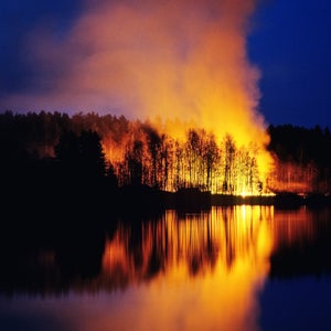 Trees on fire at night reflect in a placid lake.