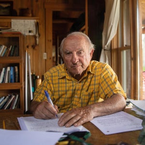 Man in yellow shirt sitting at a desk writing