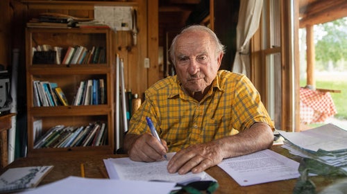 Man in yellow shirt sitting at a desk writing