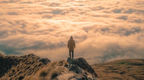 Person standing on mountain over clouds