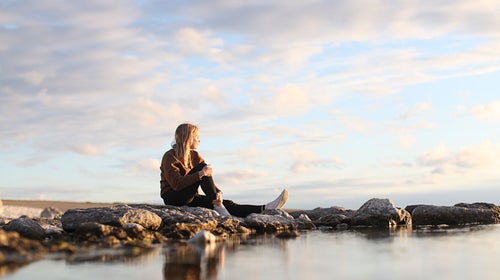 Woman looks off into the distance while sitting on a rock