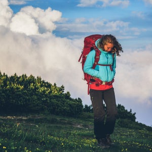 A woman cries while hiking in green tundra terrain.