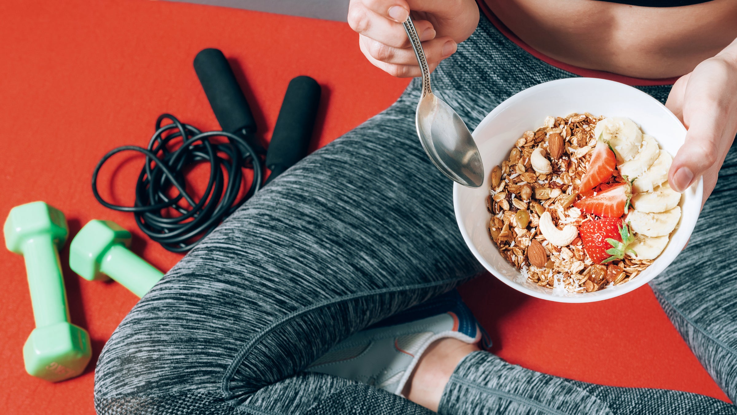 girl in sports clothes sitting near dumbbells and skipping rope with a plate of healthy breakfast in her hands to help with an upset stomach during a workout