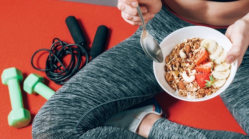 girl in sports clothes sitting near dumbbells and skipping rope with a plate of healthy breakfast in her hands to help with an upset stomach during a workout