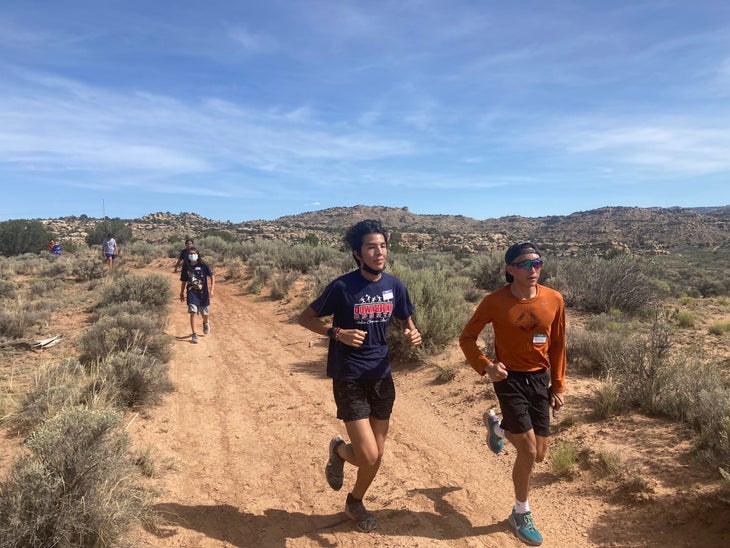 A group of runners pass along a dirt track through a desert environment