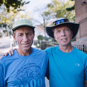 Two runners in blue shirts have arms around each other at the race