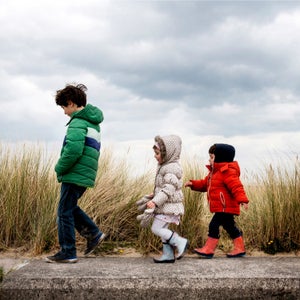 Three kids walking in puffy jackets on the beach