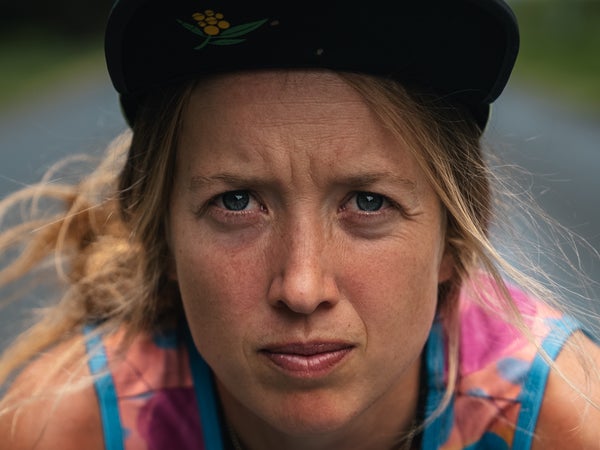 a female runner with a hat on wears pink singlet and looks into the camera