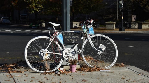 A white ghost bike leans against a streetlight. It bears a sign that says 