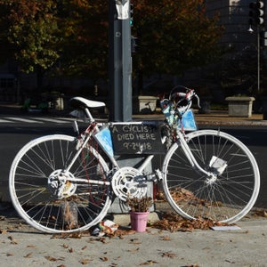 A white ghost bike leans against a streetlight. It bears a sign that says