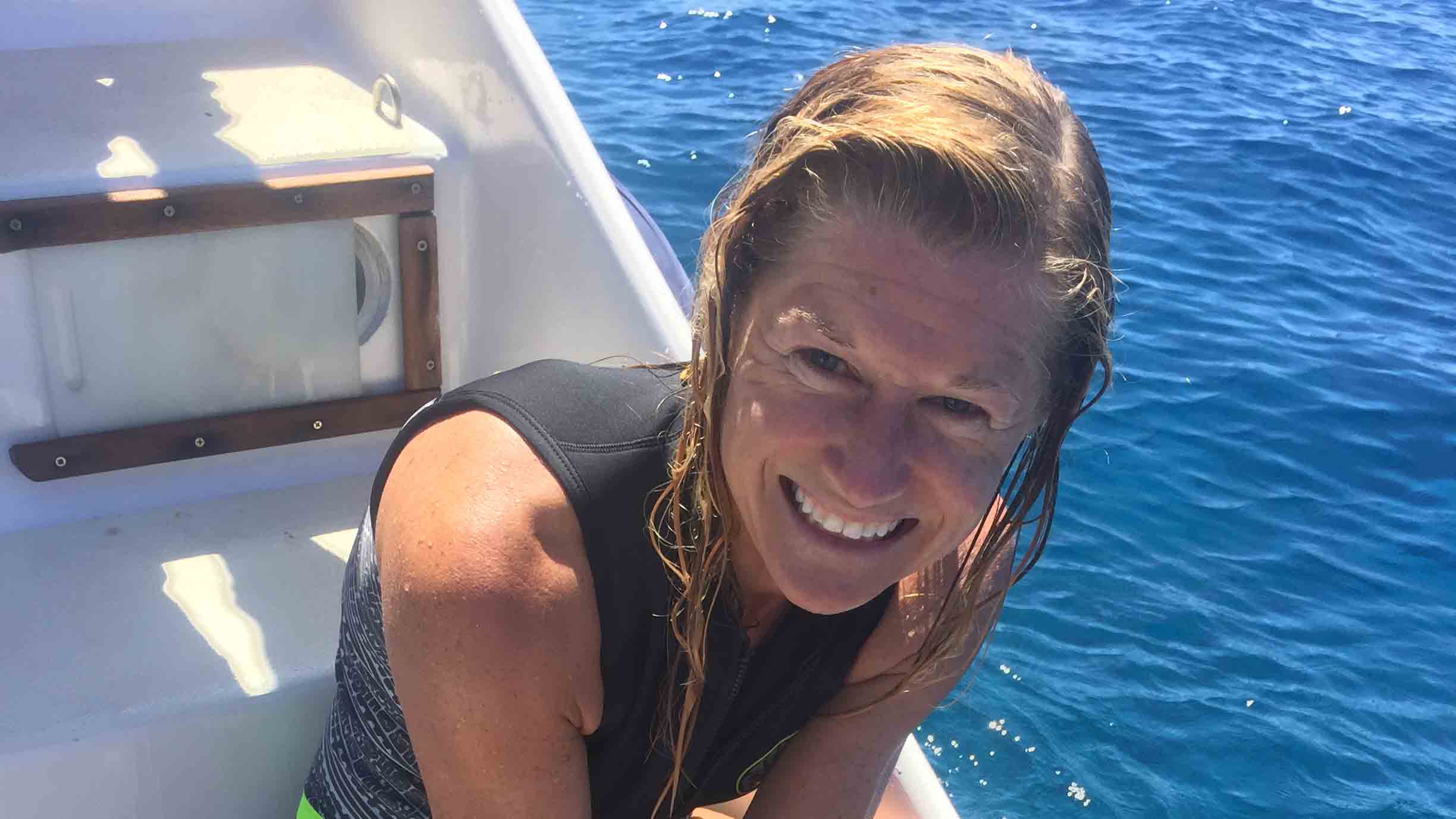 The author, wearing a wetsuit, smiles happily from her seat on a boat out in the ocean.