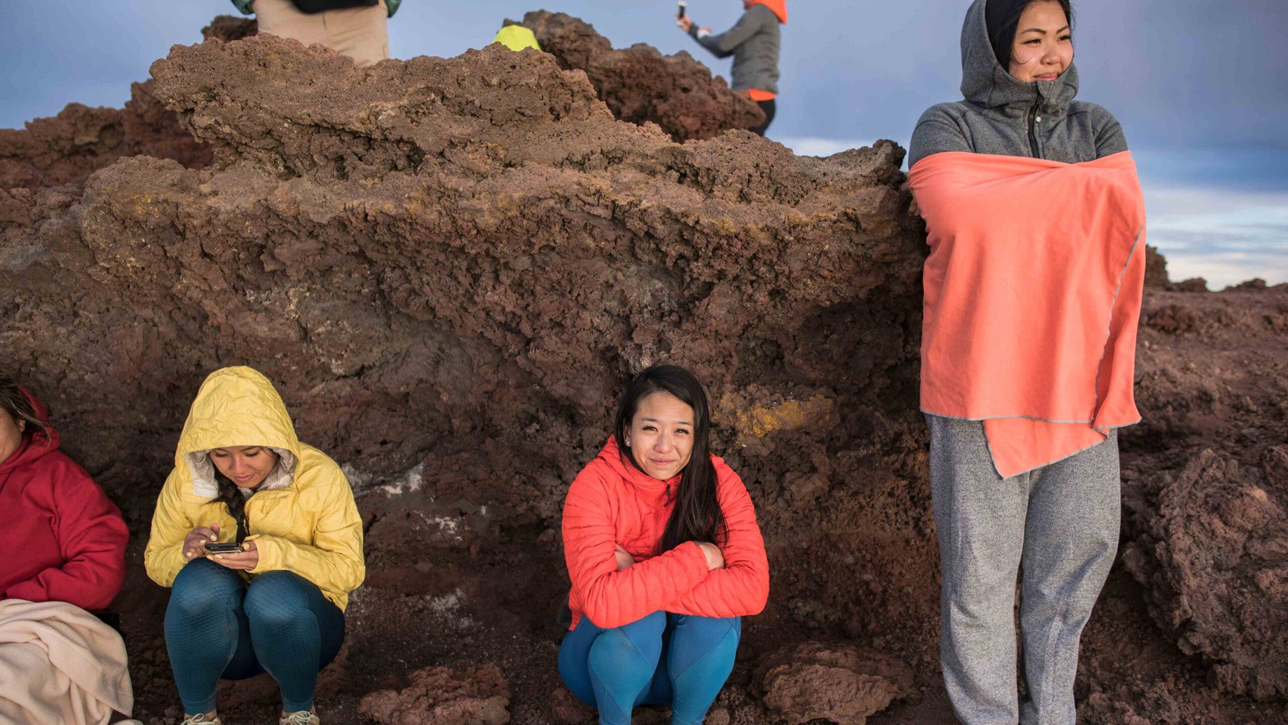 Four women wearing jackets and a blanket await sunrise at Haleakala National Park