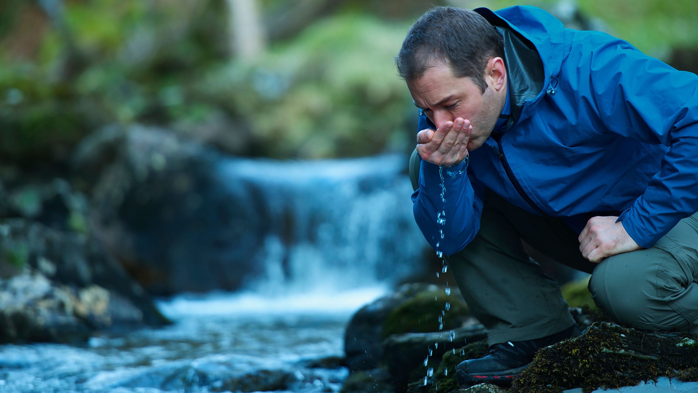 Hiker drinks from a river.