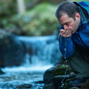 Hiker drinks from a river.