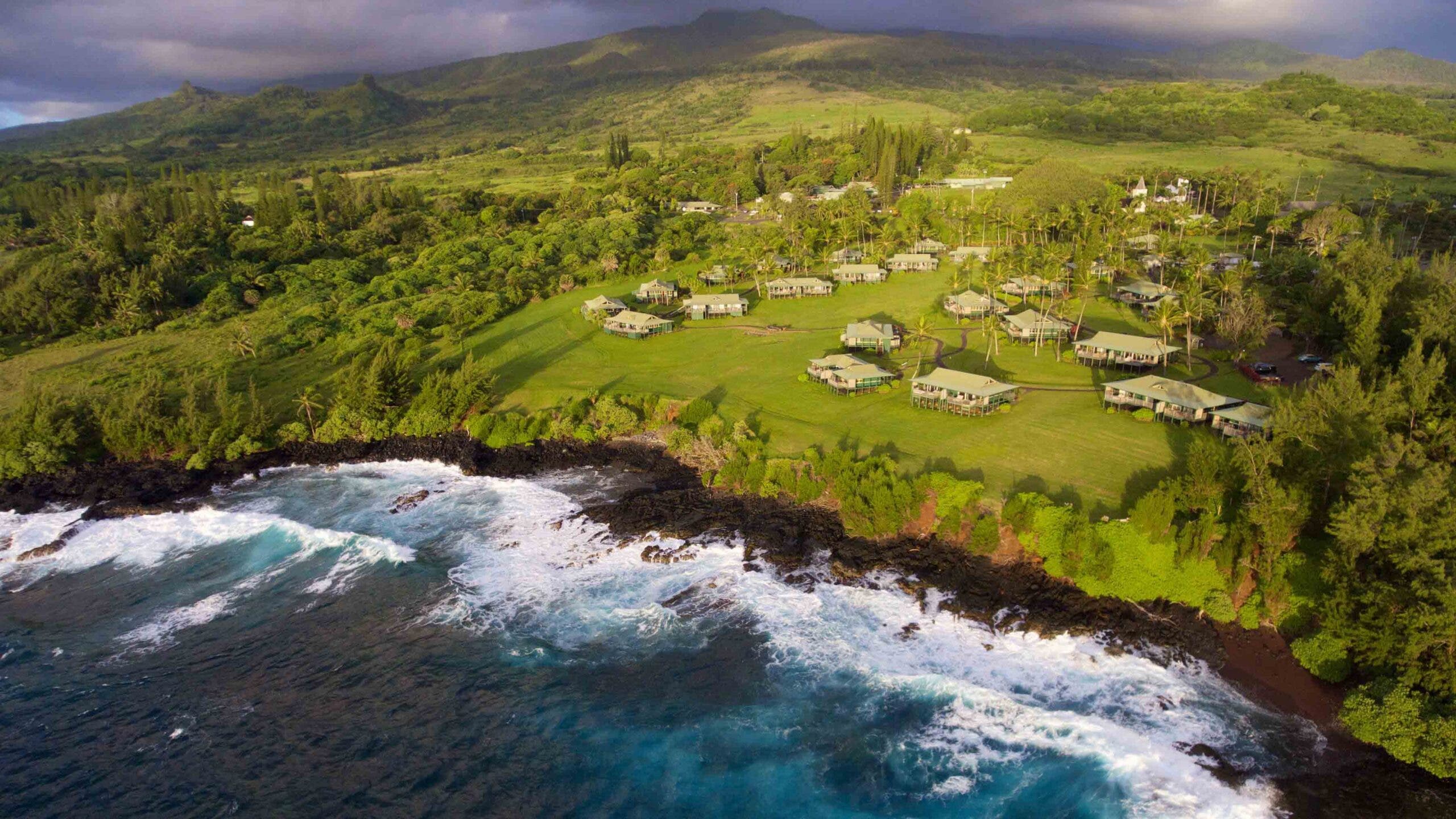 An aerial view of the lush Hana-Maui Resort property and crashing waves on its nearby shoreline
