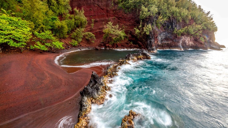 A red beach with vibrant green foliage meets beautiful blue seas on the road to Hana.