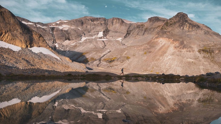 A runner makes his way along a mountain ridge with water and mountains