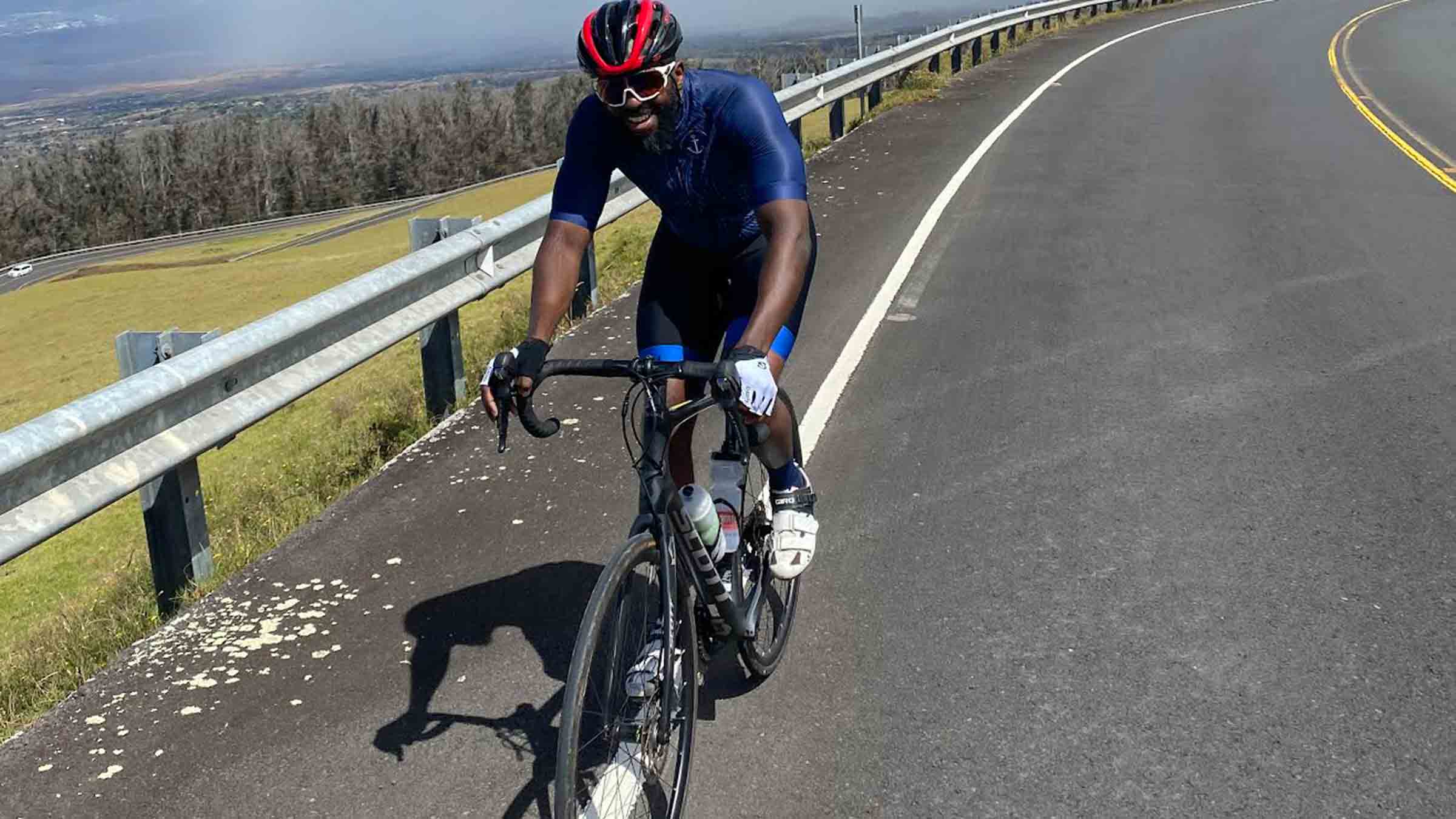 A smiling man on road bike heads downhill on the side of a blacktopped road on Maui.