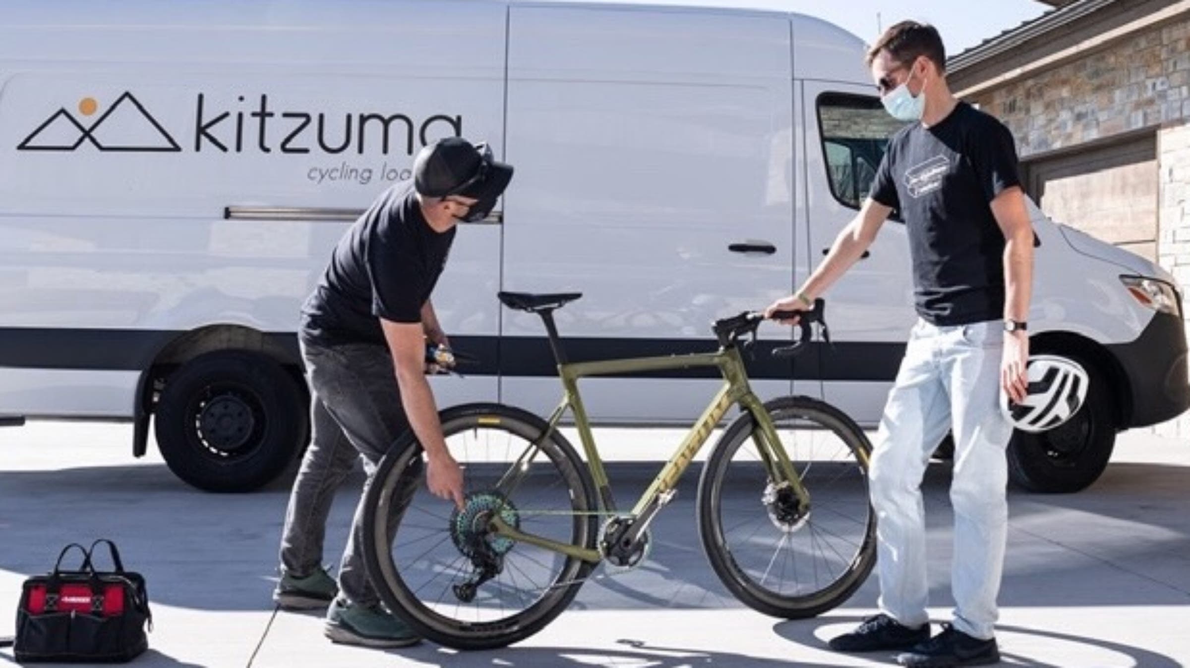 Two men with a green bicycle standing in front of white van