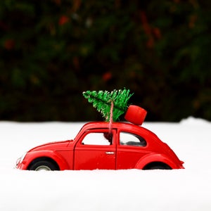 Red toy car with a christmas tree tied to the roof on a snowy winters day