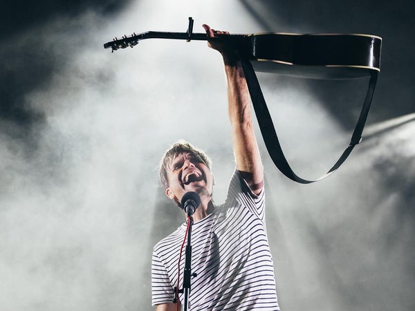 A musician holds up his guitar on stage to a smoke filled background