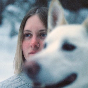 A closeup of a white dog in front of a woman in a snowy setting