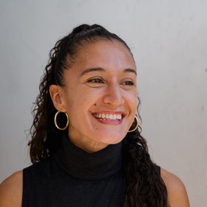 A portrait of a woman with dark hair, smiling, looking right, with a black shirt on.