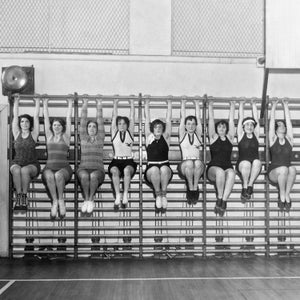 Vintage black and white photo of women in a gym doing arm hangs