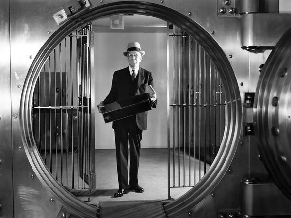 Vintage black and white photo of a man holding a box behind a bank vault door