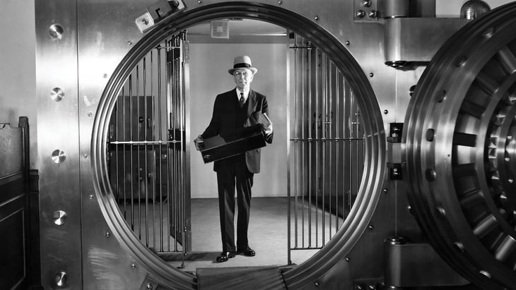 Vintage black and white photo of a man holding a box behind a bank vault door