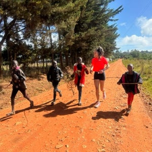 a woman in a red shirt runs with four younger children on a dirt track in Kenya
