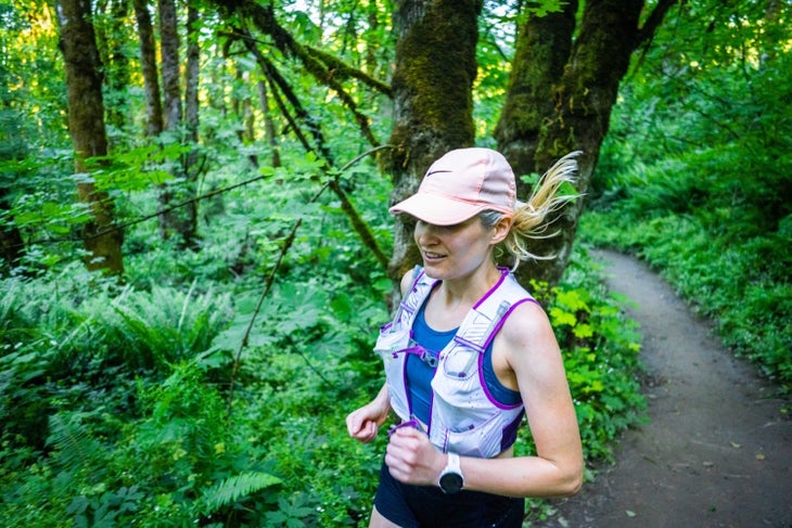 A woman with a pink hat runs through a green forest on singletrack.