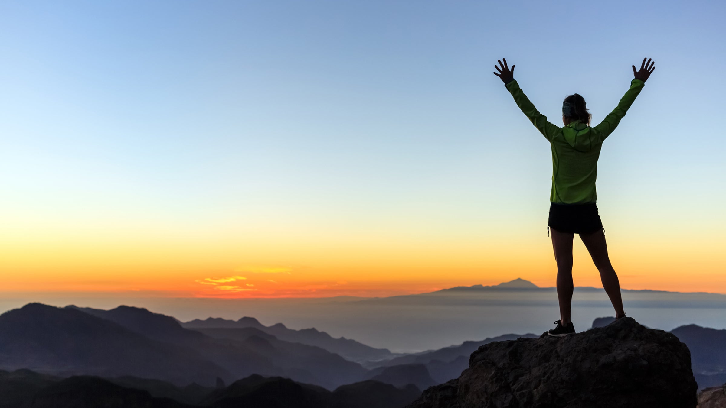 hiker with arms up outstretched on mountain top looking at view