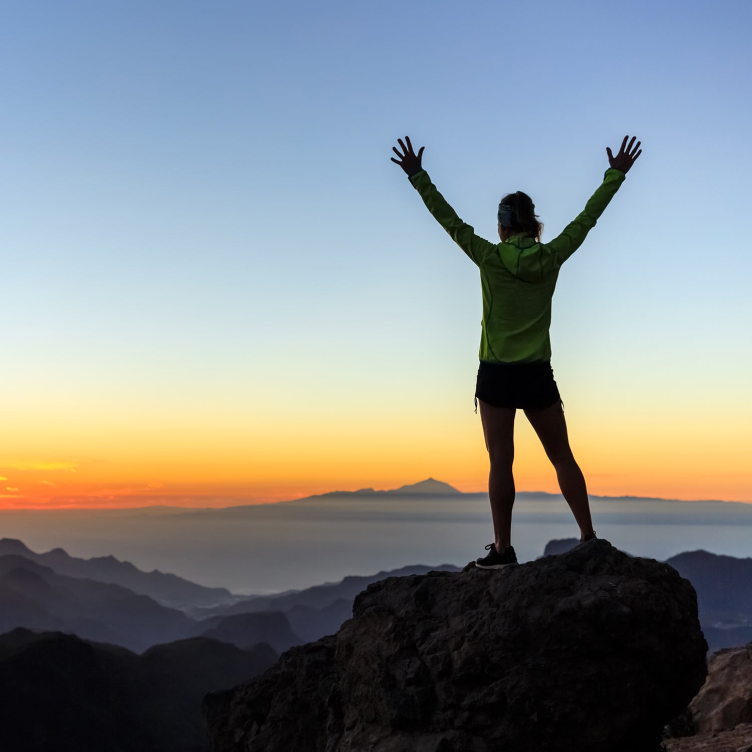 hiker with arms up outstretched on mountain top looking at view