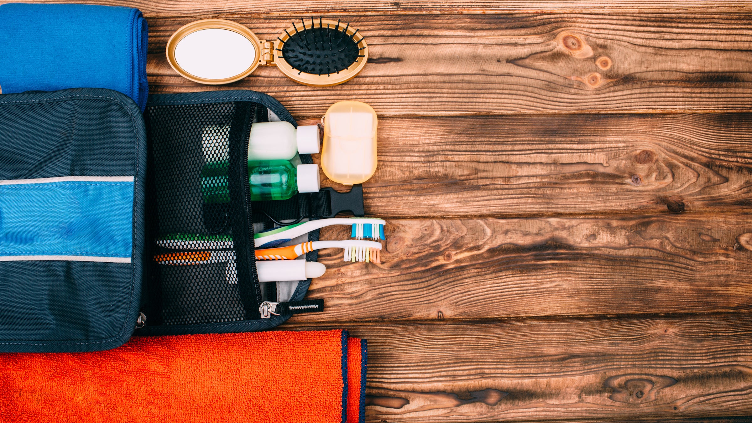 Top view of kit for hygiene during hiking and travel on wooden table with empty space. Items include towel, comb, soap, toothbrushes, shampoo